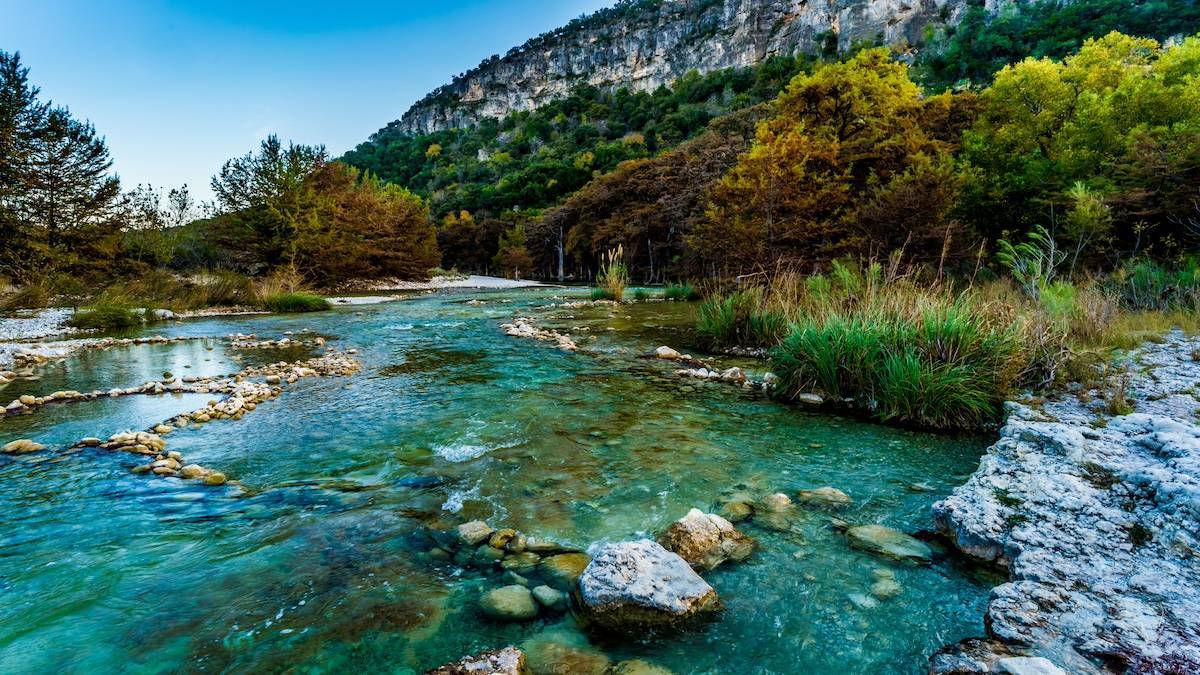 crystal clear river flowing with trees and a bluff in the background